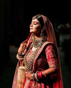 a woman in a red and gold bridal gown with jewelry on her neck, standing outside