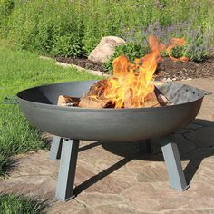 an outdoor fire pit sitting on top of a stone patio next to grass and flowers