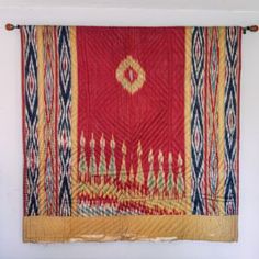 a red and yellow wall hanging on the side of a white wall next to a bed