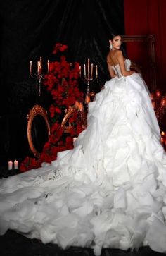 a woman in a white wedding dress sitting on a chair with red roses and candles behind her