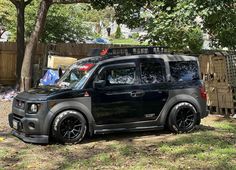 a small black car parked in front of a tree and fenced area with trees