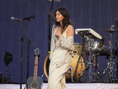 a woman standing in front of a microphone next to a guitar and drums on a stage