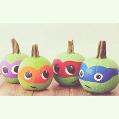 four painted pumpkins with different colored faces on them, sitting on a wooden table