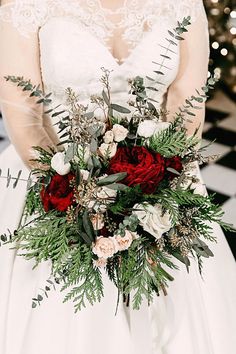 a bride holding a bouquet of flowers and greenery on her wedding day in front of a christmas tree