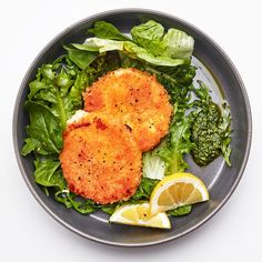 two pieces of fried fish on a bed of greens and lemon wedges next to a slice of broccoli