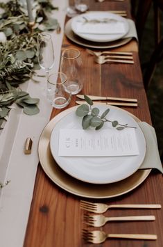 the table is set with gold and white plates, silverware, and greenery