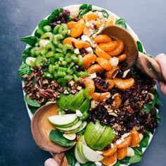 a person holding a wooden spoon over a large salad with oranges and green beans