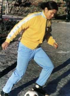 a man is kicking a soccer ball on the street while wearing blue jeans and a yellow jacket