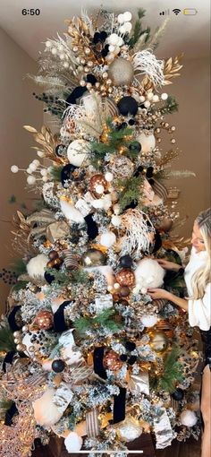 a woman standing next to a christmas tree with gold and black ornaments on it's branches