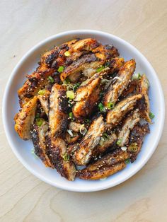 a white bowl filled with chicken wings and garnished with green onions on top