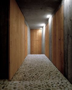 an empty hallway with wooden walls and concrete flooring is lit by recessed lights