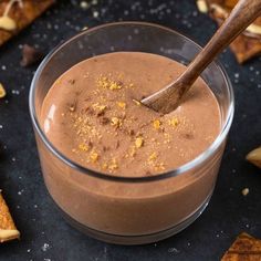 a glass bowl filled with chocolate pudding on top of a black table next to crackers