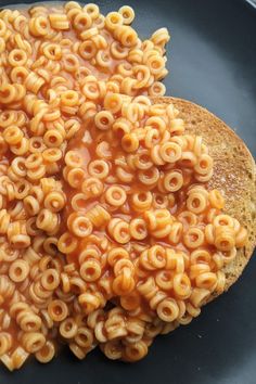 a black plate topped with macaroni and cheese next to a piece of bread