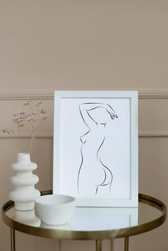 a white vase sitting on top of a glass table next to a framed nude figure