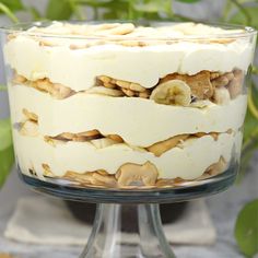 a layered cake with bananas and nuts in it on a glass stand next to a potted plant