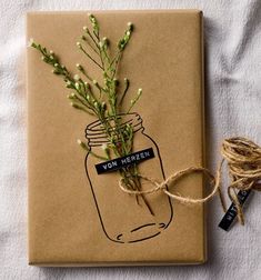 a wrapped gift with a plant in a mason jar on it and twine tied around the top