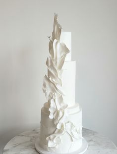 a three tiered white wedding cake on a marble table with an artistically designed topper