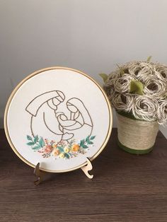 the embroidery is next to a potted plant and a small vase with flowers in it