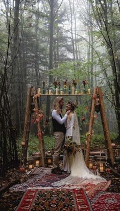 a bride and groom standing in front of a wooden arch with candles on it, surrounded by trees