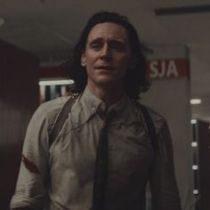 a man with long hair wearing a tie and suspenders standing in an office hallway