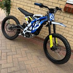 a blue and white dirt bike parked next to a brick wall