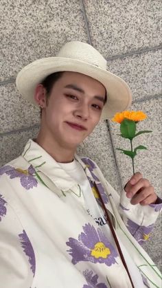 a woman wearing a white hat and holding an orange flower