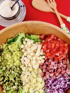 a wooden bowl filled with chopped vegetables next to spoons and utensils on a red table