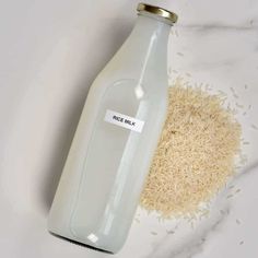 a bottle of rice milk next to a pile of white rice on a marble surface