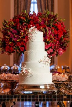 a white wedding cake sitting on top of a table next to red and pink flowers