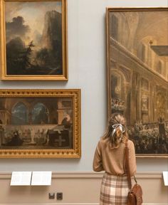 a woman looking at paintings on display in a museum