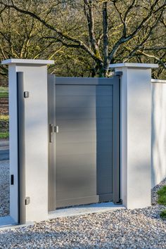 an open gray door in the middle of a graveled area with trees behind it