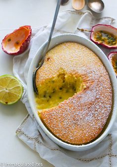 a cake in a white dish with a slice cut out and surrounded by other fruit