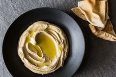 a black plate topped with hummus and tortilla chips on top of a table