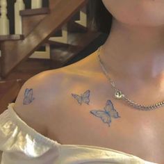 a woman with butterfly tattoos on her chest and shoulder, standing in front of stairs