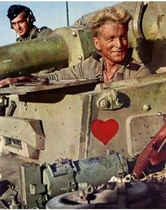 two men are sitting in the back of a tank with a heart painted on it