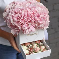 a woman holding a box filled with chocolate covered strawberries and pink hydranges