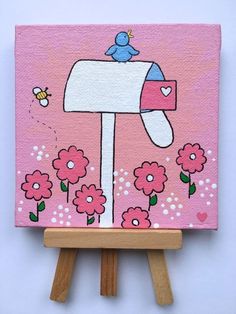 a pink painting with flowers and a bird on it's head is sitting on a small easel