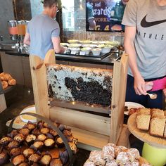 two people standing in front of a buffet filled with pastries