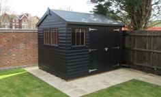 a black shed sitting in the middle of a yard next to a brick wall and fence