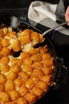 a skillet with some tater tots in it and someone holding a spoon