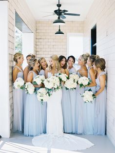 a group of women standing next to each other in front of a wall holding bouquets