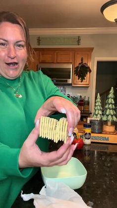 a woman in a green shirt is holding crackers and a bowl with some food on it