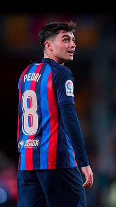 a soccer player in blue and red uniform standing on the field with his mouth open