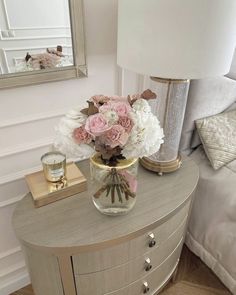 a vase filled with pink and white flowers on top of a dresser next to a mirror