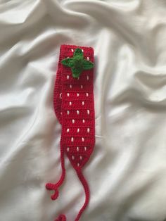 a crocheted strawberry hat laying on top of a white bed sheet with a green leaf sticking out of it