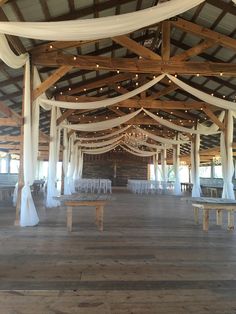 an indoor wedding venue with white draping and wooden benches in the center, surrounded by string lights