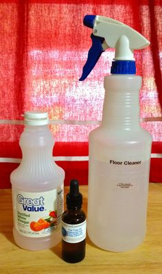 two bottles and a spray bottle sitting on a table next to a window with red curtains