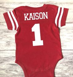 a baby bodysuit with the number one on it, sitting on a wooden floor