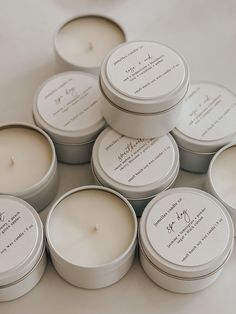 six white candles sitting on top of each other in tins next to each other