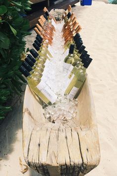 several bottles of wine sitting on top of a wooden bench in the sand near some bushes